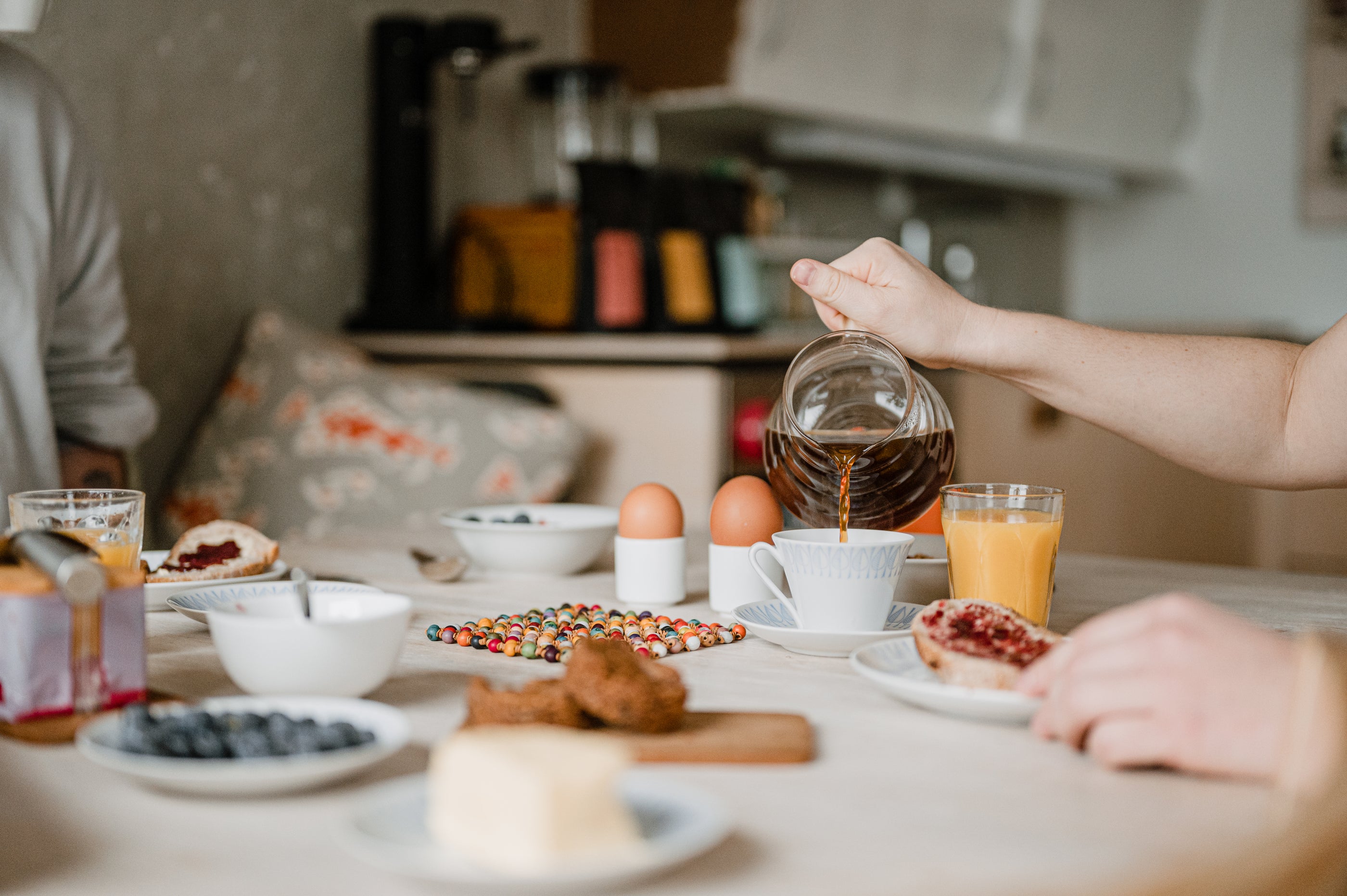 Person pouring coffee into a cup on a kitchen counter with breakfast items.